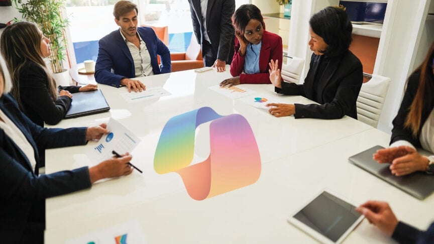 A diverse group of professional colleagues in a bright, modern office conference room, collaborating around a white table. A large, stylized Microsoft Copilot logo is superimposed in the center of the table, symbolizing AI-driven teamwork and productivity.